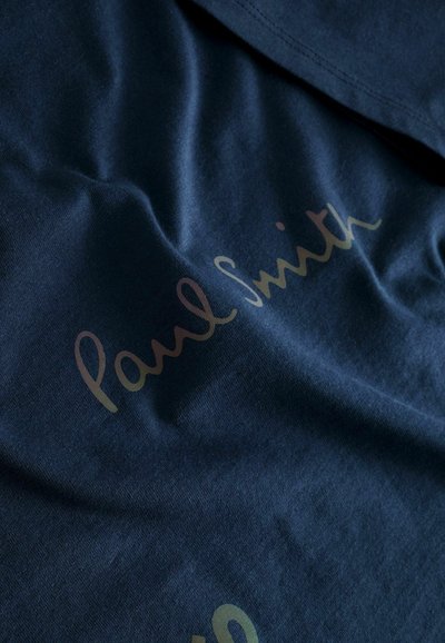 Marinblå t-shirt i bomull med en slät textur, med texten "Paul Smith" i gradienttryck på framsidan.