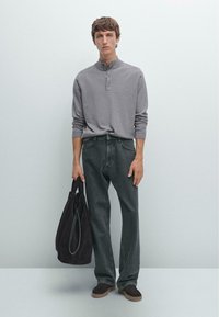 Grå långärmad henley-tröja med knapplist, kombinerad med mörkgrå vida jeans. Håller en svart mocka tote-väska. Bruna träskor.