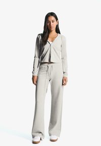 Világosszürke két részes otthoni viselet szett, puha anyagból készült. Jellemzője a zippzáros, rövidített kapucnis pulóver és a bővülő szárú nadrág, mindkettő laza szabású.