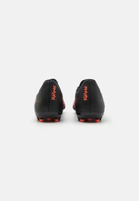 Botas de fútbol negras con acentos rojos, superficie texturizada y diseño curvado; con suela de múltiples tacos para una buena tracción.