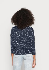 Top padrão azul-marinho com mangas três quartos, apresentando um print abstrato branco; usado com jeans desbotados azul-claro.