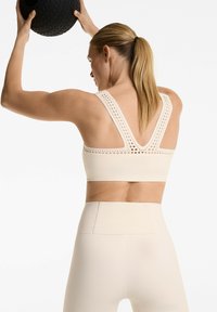 Beige athletic crop top with lace-like cutouts on wide straps, paired with high-waisted leggings in matching color, smooth texture.