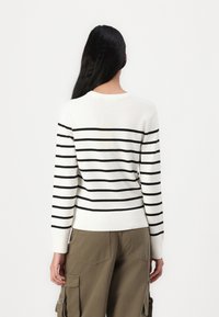 Pull rayé avec une base blanche et des lignes horizontales noires, poignets côtelés et col rond ; porté avec un pantalon cargo olive.