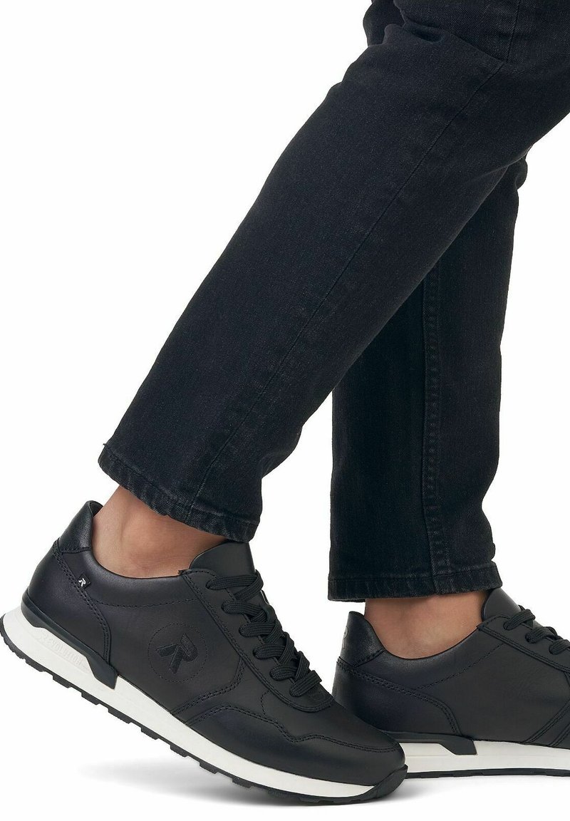 Basketball en cuir noir avec une finition texturée, semelle intermédiaire blanche et logo discret sur les côtés. Portées avec un denim foncé.