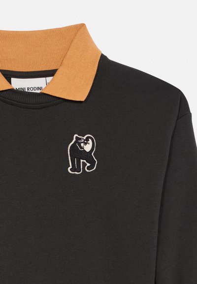 Sweat-shirt noir avec col côtelé jaune moutarde et logo brodé de chat noir sur la poitrine, étiquette de la marque Mini Rodini visible à l'intérieur du col.