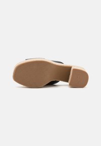 Zapato de tacón negro con una plataforma de corcho texturizado y suela antideslizante. Presenta un upper de cuero suave y un diseño de punta redondeada.