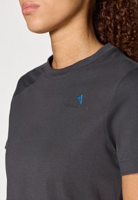 Sötét szürke, testhezálló póló kerek nyakkivágással, rövid ujjakkal és a bal felső mellen kék hímzett logóval. Simább pamut textúra.