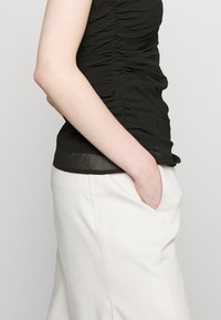 Μαύρη, ρυγχωτή, αμάνικη μπλούζα συνδυασμένη με ανοιχτό μπεζ, ψηλόμεσο παντελόνι με πλαϊνές τσέπες. Μαλακό ύφασμα με λεία υφή.