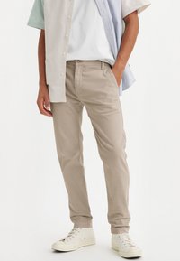 Beige chinos gjorda av mjuk bomull, med slim fit, sidofickor och en något avsmalnande ben, i kombination med vita sneakers.