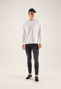 Langärmliges weißes Hemd, figurbetonte schwarze Jeans, schwarze Turnschuhe mit weißen Akzenten, schwarze Kappe; glatte Textur, minimalistisches Design.