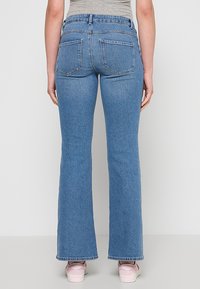 Svetlo modre kavbojke z razširjenimi hlačnicami, srednje visokim pasom, dvema zadnjima žepoma in gladko teksturo. Kombinirane s svetlimi čevlji.