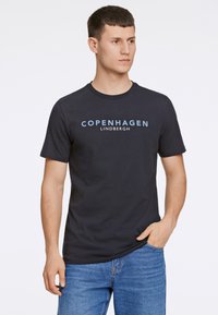 Marineblauwe katoenen t-shirt met korte mouwen, ronde hals, met de tekst "COPENHAGEN LINDBERGH" in lichtblauw langs de voorkant.