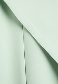 Jasnozielony materiał o gładkiej fakturze i wyraźnym ukośnym fałdzie, z czystymi szwami wzdłuż krawędzi oraz subtelnym połyskiem.