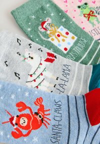 Colorful knitted socks featuring holiday designs: a mouse, llama, frog, and Santa Claws, in green, gray, pink, and blue with patterned accents.