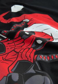 T-shirt graphique rouge et noir présentant un personnage stylisé portant un chapeau de Père Noël, avec des contours audacieux et des détails complexes.