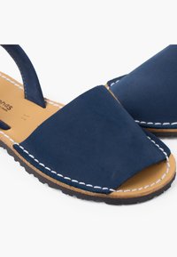 Para granatowych skórzanych sandałów z otwartym palcem, białym przeszyciem i brązową wkładką na białym tle.