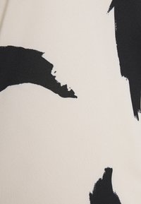 Látka s krémovým základem a velkými, abstraktními černými tahy barvy. Textura vypadá tkaná, s mírně strukturovaným povrchem.