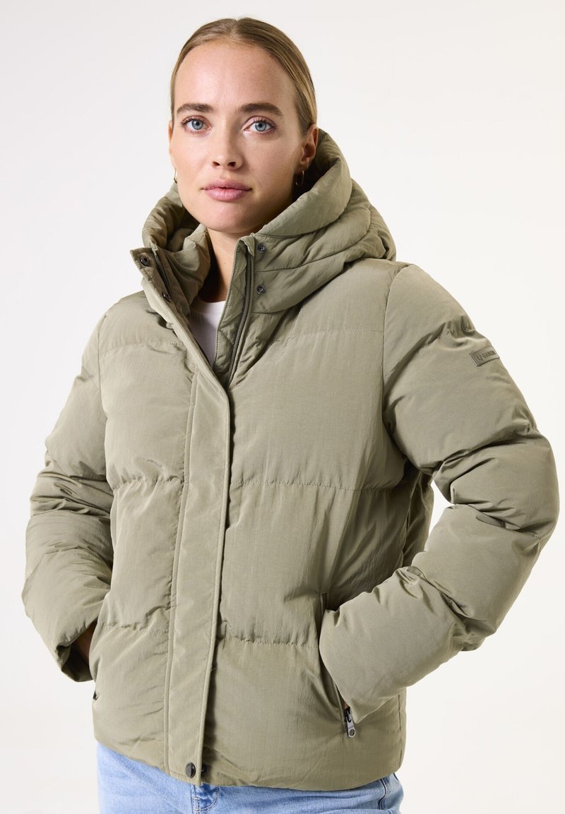 Chaqueta acolchada en verde oliva claro, cuenta con una capucha, cierre frontal con cremallera, puños elásticos y bolsillos laterales con un acabado suave y texturizado.