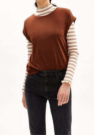 Brun kortærmet top lagdelt over en langærmet skjorte med striber, kombineret med højtaljede sorte jeans. Tekstureret stof med en afslappet pasform.