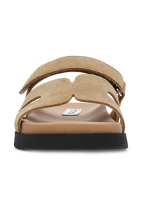 Le ciabatte in suede color tan presentano due ampie cinghie con disegni ritagliati, una suola interna beige liscia e una suola in gomma nera.