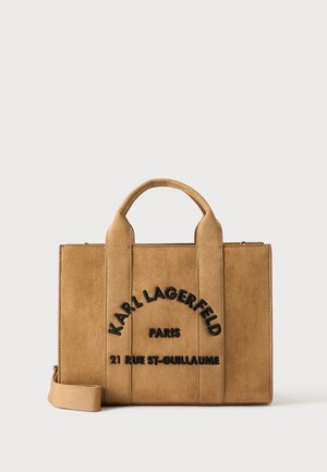 Rettangulær taske i tan ruskind med top håndtag og sort tekst med teksten Karl Lagerfeld Paris 21 Rue St-Guillaume foran.