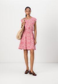 Red and white patterned dress with short sleeves, fitted waist, flared skirt, and a textured natural straw bag. Brown loafers with gold accents.
