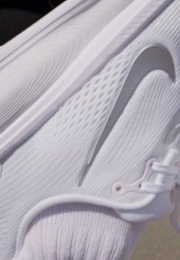 Baskets blanches avec tige texturée, design courbé, grand swoosh argenté et système de laçage élastique. Semelle lisse avec motif strié.
