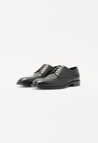 Le scarpe da uomo in pelle nera presentano una punta arrotondata, un design con lacci, una superficie liscia e un tacco basso impilato.