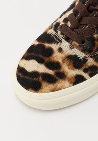 Sneakers w print w panterę, z fakturowaną futrzaną cholewką, ciemnobrązowymi sznurówkami i kremową gumową podeszwą. Dodatki obejmują detal szycia.