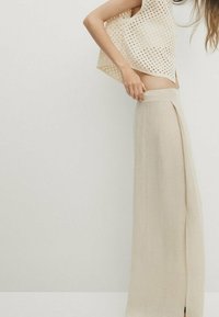 Beige Leinen-Weitbein-Hosen mit einem leichten Schlitz vorne, kombiniert mit einem locker gestrickten creamfarbenen Oberteil mit einem durchbrochenen Design.