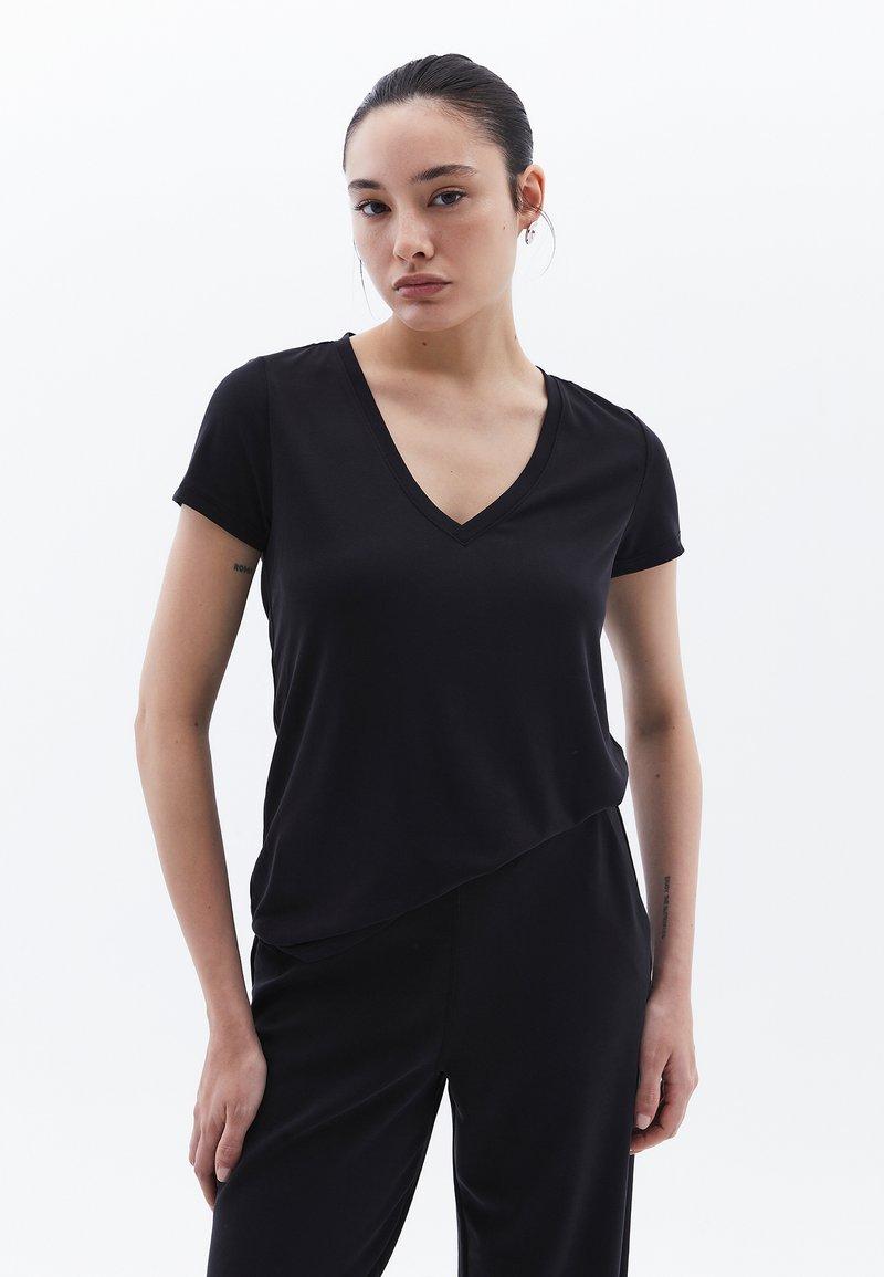 T-shirt nera con scollo a V, maniche corte, una texture liscia e un'orlo asimmetrico, abbinata a pantaloni neri coordinati.