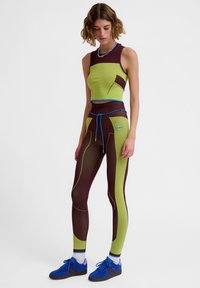 Sportstøj med en grøn crop top og brune leggings med kontrastfarvede blå detaljer, lavet af strækbart materiale, der fremhæver indviklede mønstre.