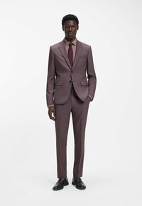 Brauner Karoanzug, maßgeschneiderte Passform, mit Kerbkragen, zwei Knöpfen und flachen Vorderhosenteilen. Kombiniert mit einer passenden Krawatte und schwarzen Schuhen.