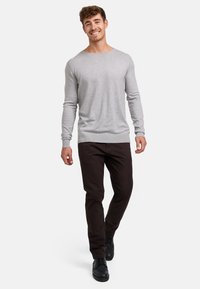 Suéter gris de manga larga con un cuello de canalé, combinado con pantalones marrón oscuro y zapatos negros, con un diseño simple y ajustado.