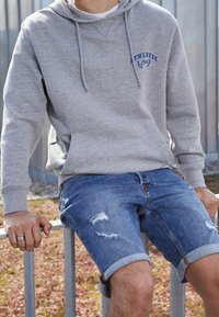 Gray hoodie with drawstrings, featuring blue text. Worn with blue denim shorts, showing distressed accents and rolled cuffs.