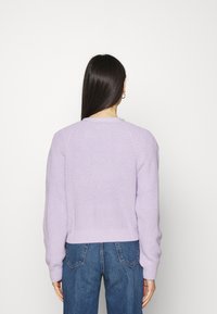 Lila stickad tröja med texturerad finish, med ribbad halsringning och muddar, ihop med högmidjade blåjeans.