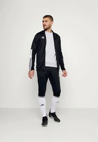 Μαύρο αθλητικό σακάκι με λευκές ρίγες, συνδυασμένο με γκρι μπλούζα και μαύρο παντελόνι. Διακοσμημένο με λευκές κάλτσες και μαύρα παπούτσια.