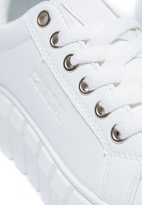 Bílé platformové tenisky z hladkého syntetického materiálu, s kovovými průchodkami, plochými tkaničkami a vyraženým logem značky na boku.