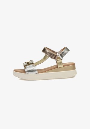 Sandal metálico de tres tiras con una suela blanca gruesa, cuenta con acentos en plata, oro y bronce, y una superficie texturizada en las tiras.