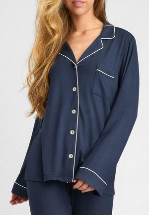 Granatowy top piżamy z długimi rękawami, perłowymi guzikami i białymi wykończeniami. Posiada kieszeń na piersi oraz luźny krój. Miękka tekstura.