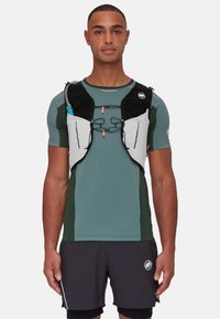 Black and gray hydration vest worn over a green athletic shirt, featuring a front pocket, adjustable straps, and water tube attachment.
