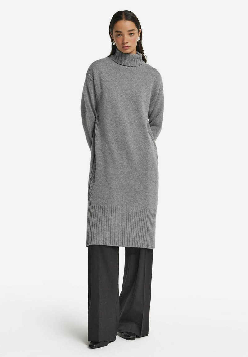 Grå polotröja i stickad klänning med ribbat fåll och sidodetaljer, parat med vida svarta byxor. Mjuk textur, oversized passform.