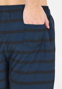 Shorts bleu marine avec des rayures horizontales noires, dotés d'une taille élastique et d'une poche arrière fermée par un bouton.