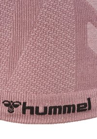 Zbliżenie różowego, dzianego materiału o zróżnicowanej fakturze z czarnym logo „hummel” wyszytym na dolnej krawędzi.