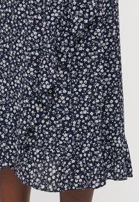 Robe florale marine avec un motif de petites fleurs blanches, en tissu léger, avec un ourlet évasé, des manches courtes, une texture subtile et une coupe décontractée.