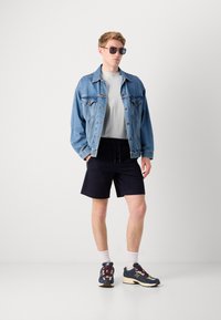 Denimjakke, lysegrå t-skjorte, svarte shorts og flerfargede joggesko med hvite sokker, som viser en uformell sommeroutfit.