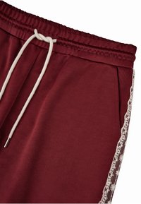 Bordo sportinės kelnės su raišteliu, su šoninėmis nėrinėmis akcentais ir glotnia tekstūra. Elastinga juosta komfortui.
