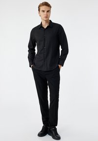 Czarna koszula z długim rękawem i kołnierzykiem, gładka w dotyku, zestawiona z czarnymi spodniami i czarnymi sneakersami. Prosty, elegancki design.