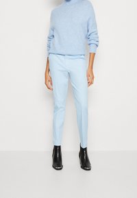 Světlé modré, upnuté kalhoty s hladkým povrchem, spárované se vzdušným, světle modrým rolákem. Černé kotníkové boty s texturovaným povrchem.