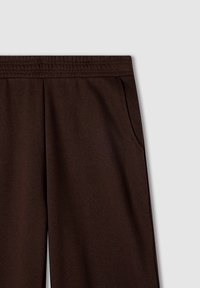 Pantaloni della tuta marroni con vita elasticizzata, tasche laterali e un tessuto morbido e texturizzato. Design semplice, senza motivi o accenti visibili.
